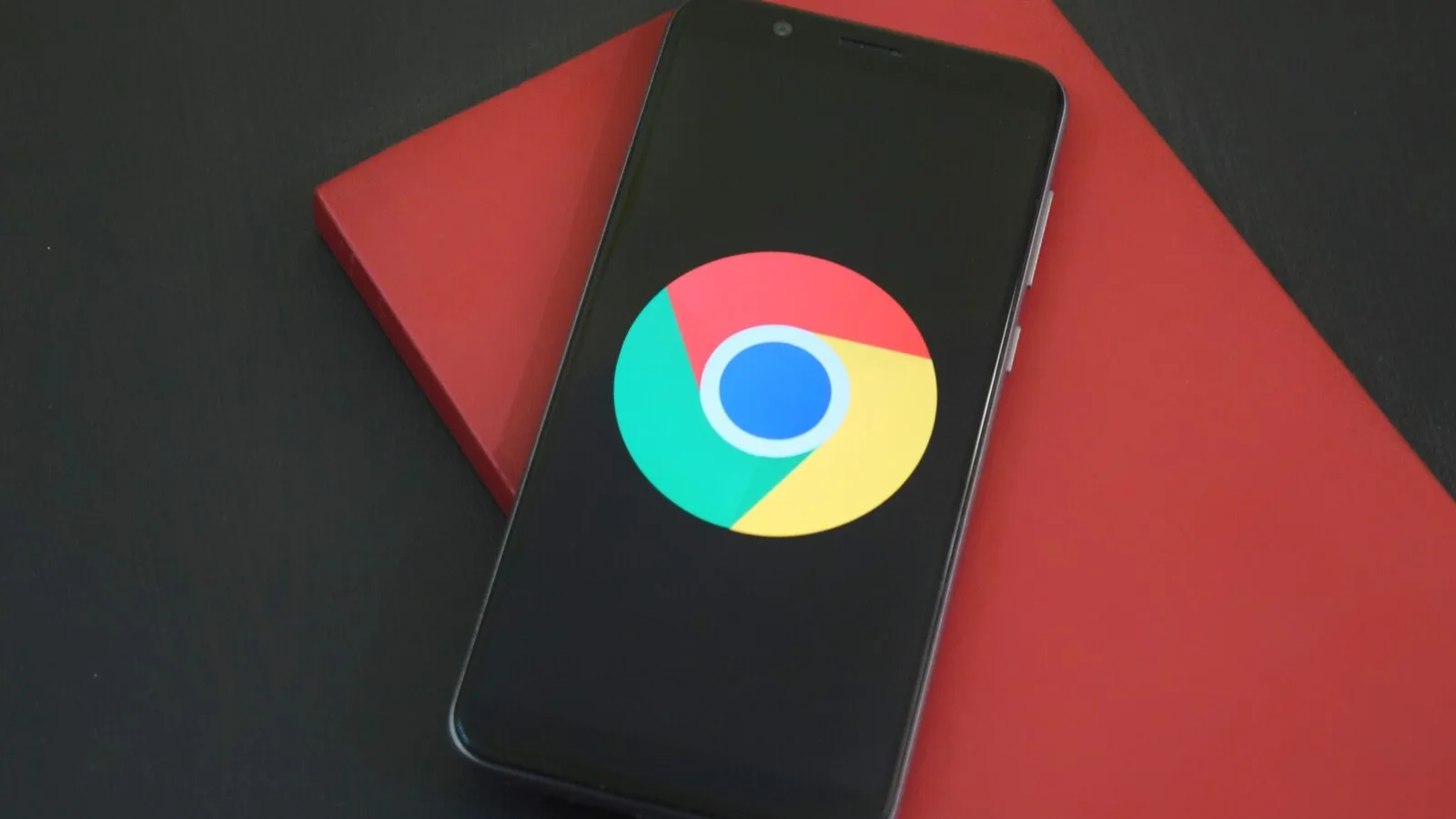 Smartphone preto pousado sobre um caderno vermelho, com o logótipo do Google Chrome no ecrã