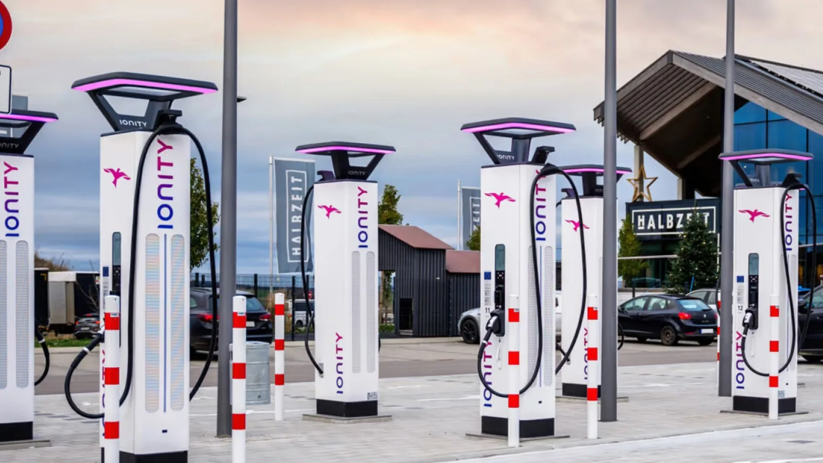 Fila de carregadores rápidos IONITY brancos com iluminação lilás, num parque de estacionamento ao fim da tarde