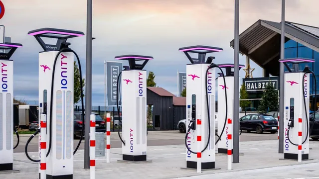 Fila de carregadores rápidos IONITY brancos com iluminação lilás, num parque de estacionamento ao fim da tarde