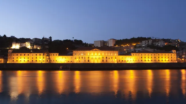 Edifício da Alfândega do Porto iluminado ao anoitecer, refletido nas águas do rio Douro