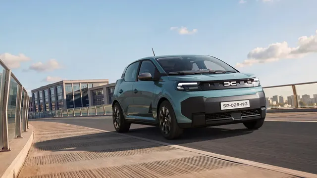 Novo Dacia Spring em verde-azulado a circular numa ponte, visto de frente a três quartos, com edifícios ao fundo