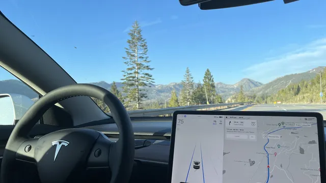 Interior de um Tesla numa autoestrada de montanha, com o volante à esquerda e o ecrã central a mostrar o carro na faixa e um mapa