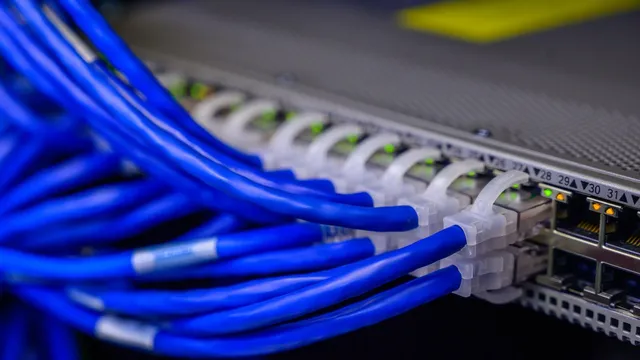 Cabos de rede azuis ligados às portas de um switch num centro de dados, com luzes verdes acesas