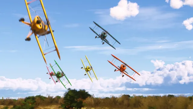 Cinco biplanos coloridos em amarelo, verde, vermelho, laranja e azul-petróleo a curvar em grupo a baixa altitude, sobre arbustos e com céu azul