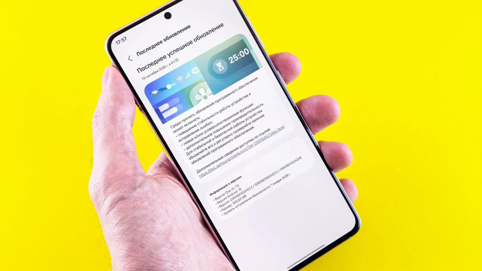Mão a segurar um telemóvel Samsung com o ecrã de atualização de software aberto, sobre fundo amarelo