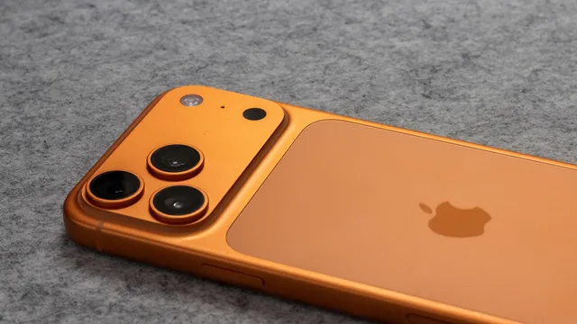Traseira de um iPhone cor de laranja com três câmaras e o logótipo da Apple, pousado sobre um tecido cinzento