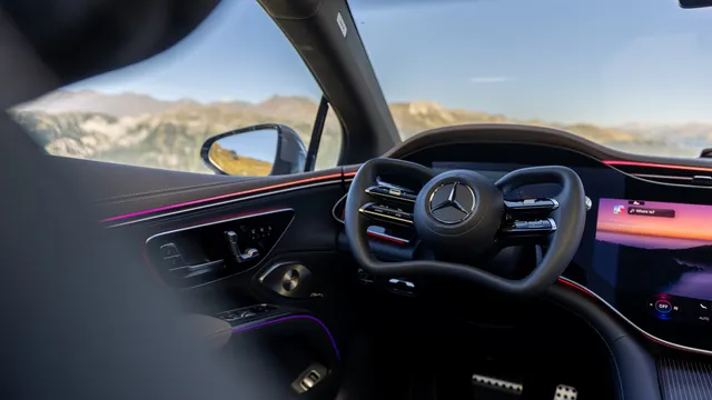 Interior do Mercedes-Benz EQS com o volante compacto em forma de yoke, o ecrã central à direita e montanhas vistas pelo para-brisas