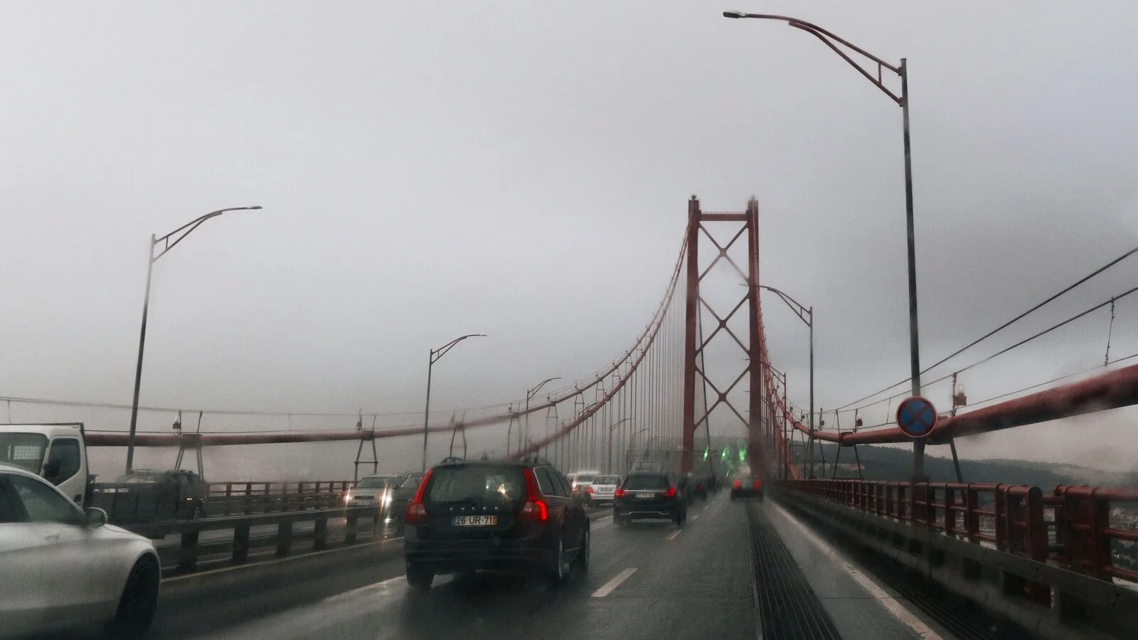 Carros a atravessar a Ponte 25 de Abril, em Lisboa, num dia de chuva e nevoeiro, vistos através do para-brisas