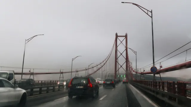 Carros a atravessar a Ponte 25 de Abril, em Lisboa, num dia de chuva e nevoeiro, vistos através do para-brisas