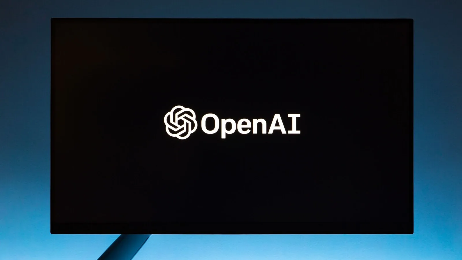 Monitor com fundo preto a mostrar o logótipo e o nome da OpenAI, iluminado por luz azul por trás