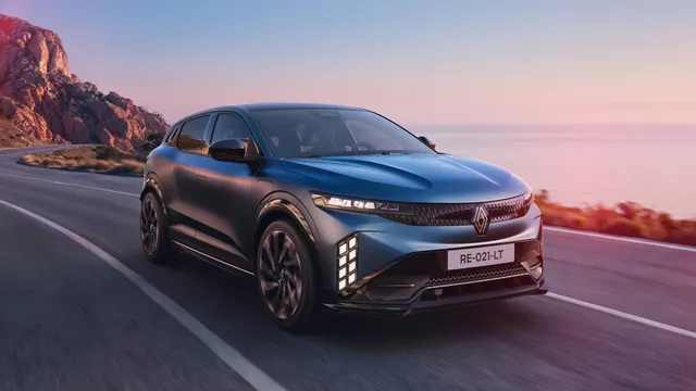 Renault Mégane E-Tech elétrico renovado, em azul escuro, a circular numa estrada junto ao mar ao pôr do sol