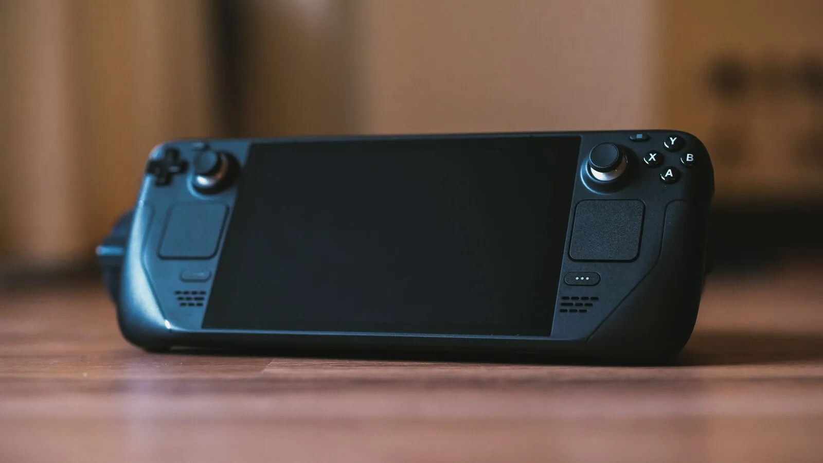 Consola portátil Steam Deck preta pousada num chão de madeira, com o ecrã desligado e o fundo desfocado