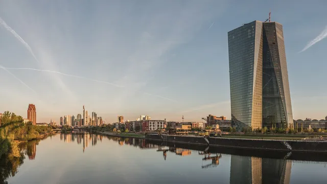Torre de vidro da sede do Banco Central Europeu junto ao rio Meno, em Frankfurt, com os arranha-céus da cidade ao fundo, ao amanhecer