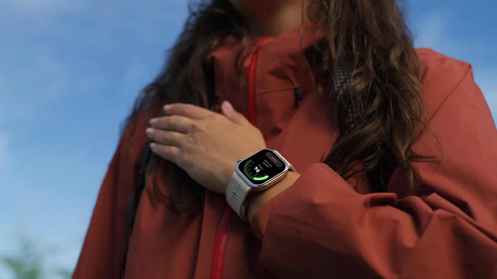 Mulher com casaco vermelho e a mão sobre o peito, com o Huawei Watch D3 de bracelete branca no pulso a mostrar uma medição em curso