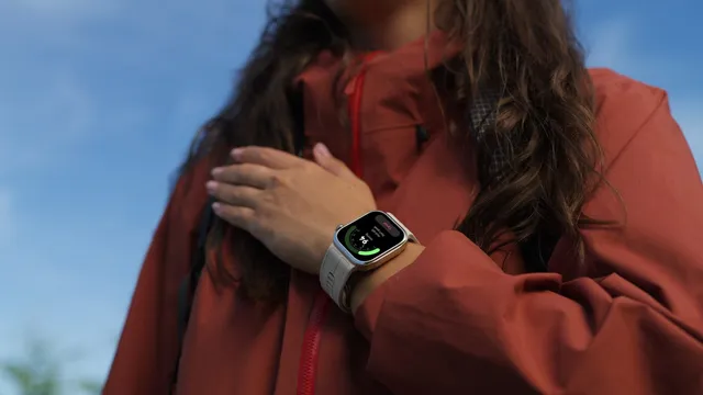 Mulher com casaco vermelho e a mão sobre o peito, com o Huawei Watch D3 de bracelete branca no pulso a mostrar uma medição em curso