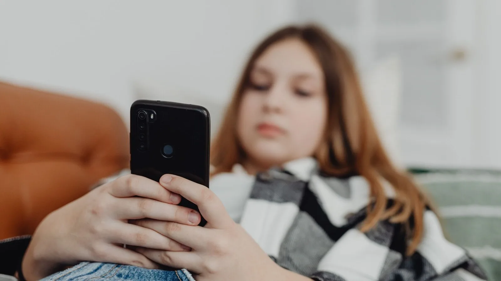 Adolescente deitada num sofá a usar o telemóvel, com o aparelho em primeiro plano