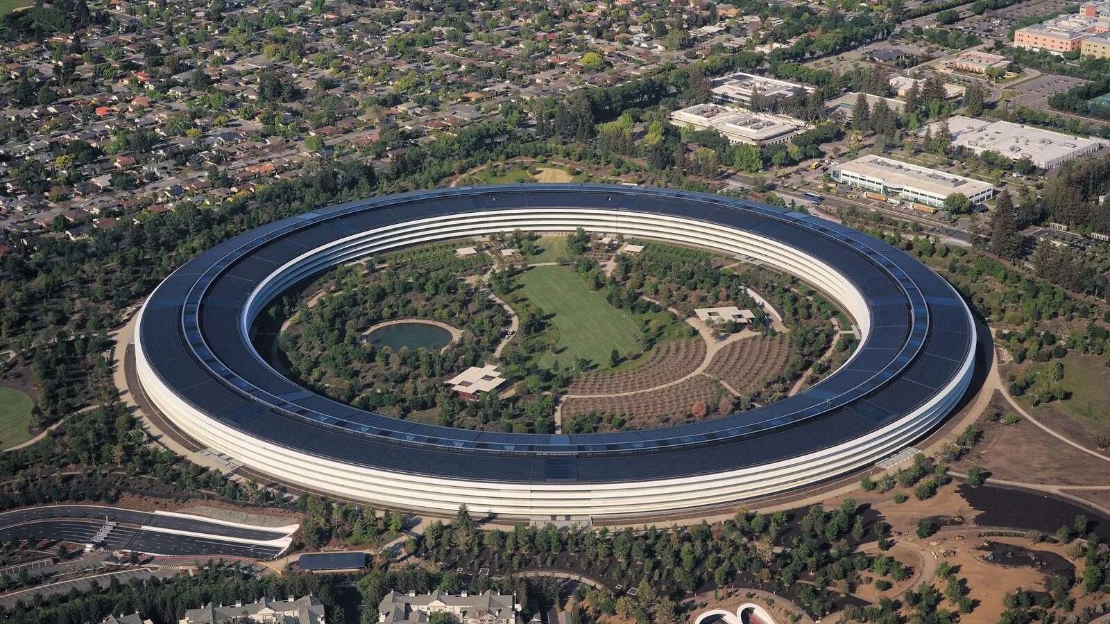 Vista aérea do Apple Park, o edifício em forma de anel da sede da Apple, rodeado de árvores e de bairros residenciais