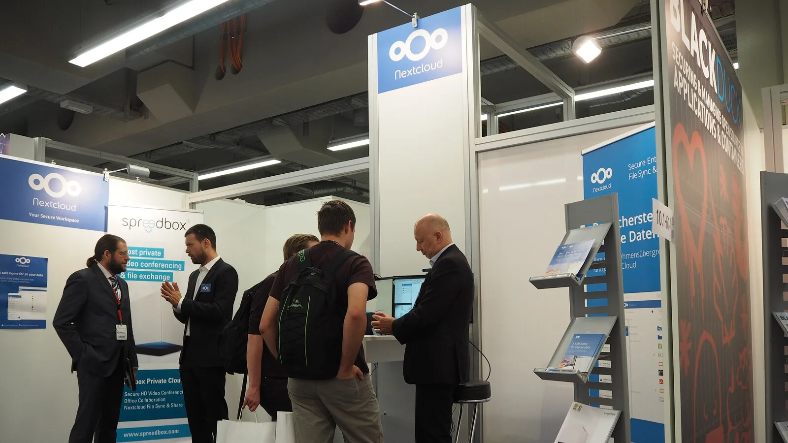 Visitantes junto ao expositor do Nextcloud numa feira de tecnologia, com o logótipo azul da marca no topo de uma coluna