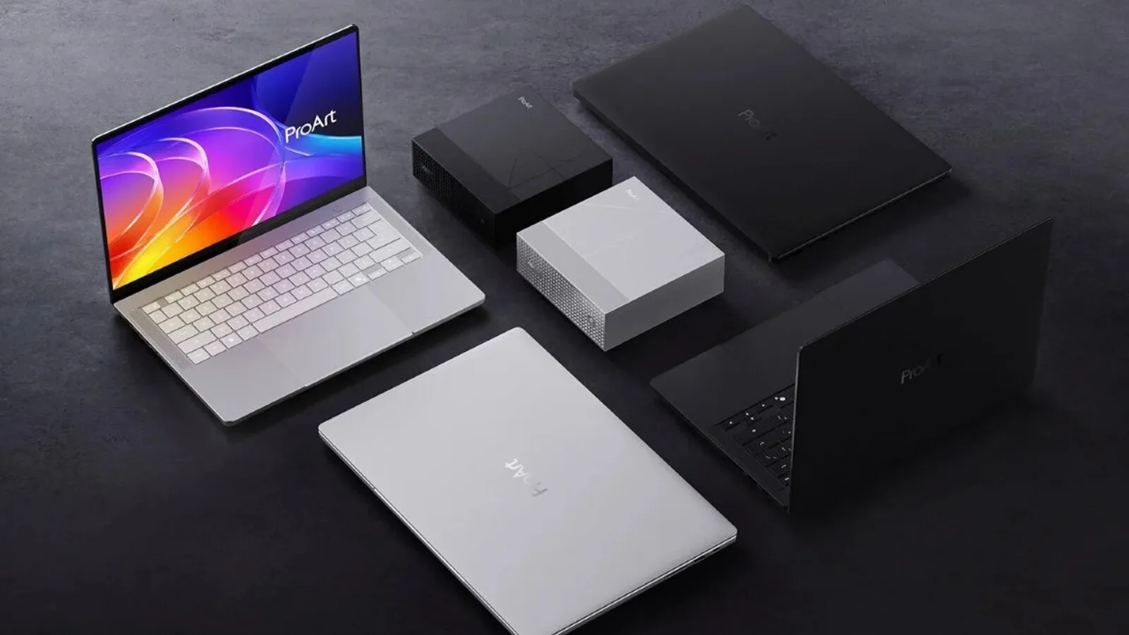 Quatro portáteis ASUS ProArt, dois prateados e dois pretos, e dois mini PC sobre uma superfície escura, um dos portáteis aberto com o ecrã colorido