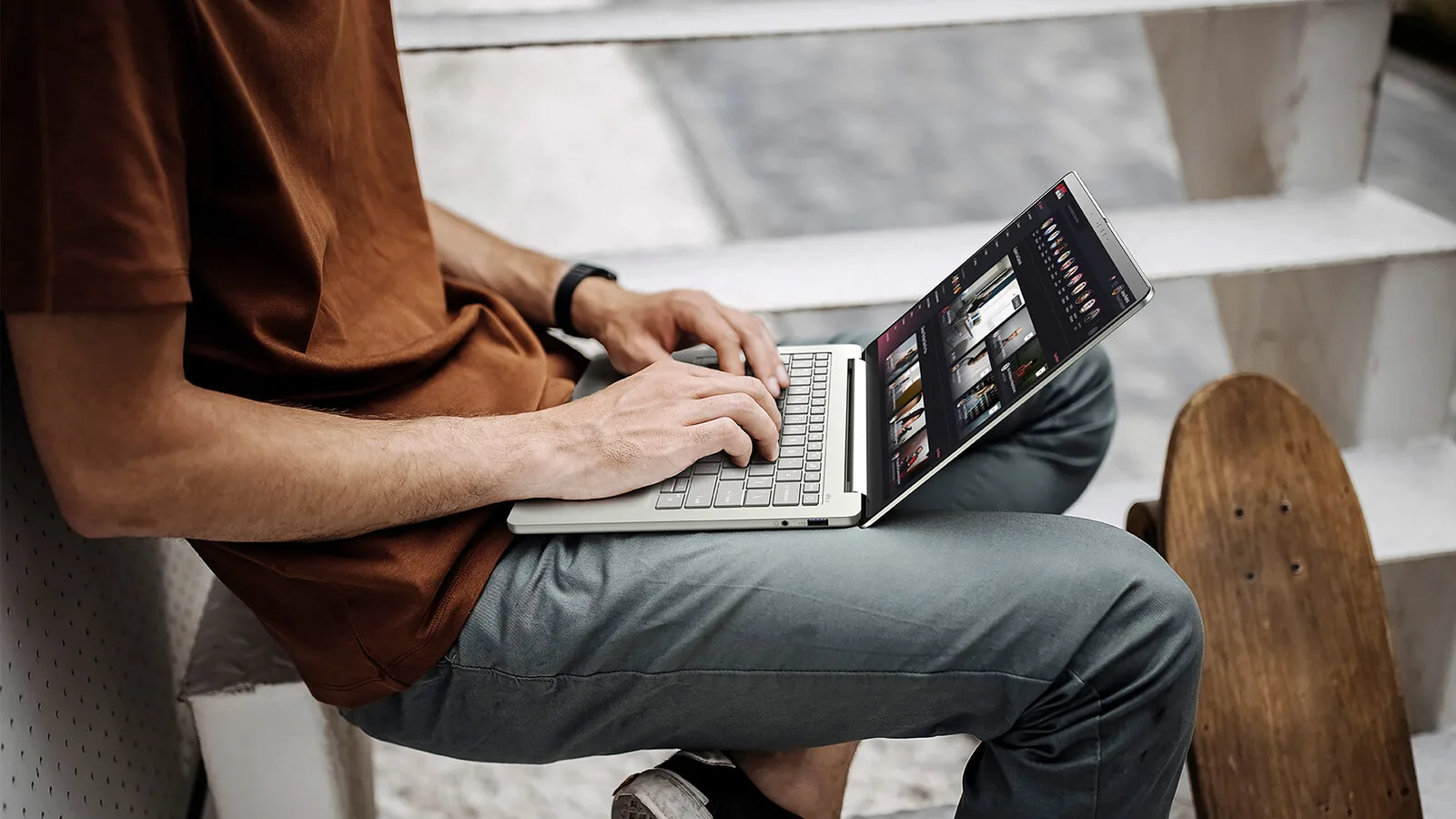 Homem sentado numa escada exterior a escrever num portátil Acer Swift Air 14 prateado pousado nas pernas, com um skate encostado ao lado