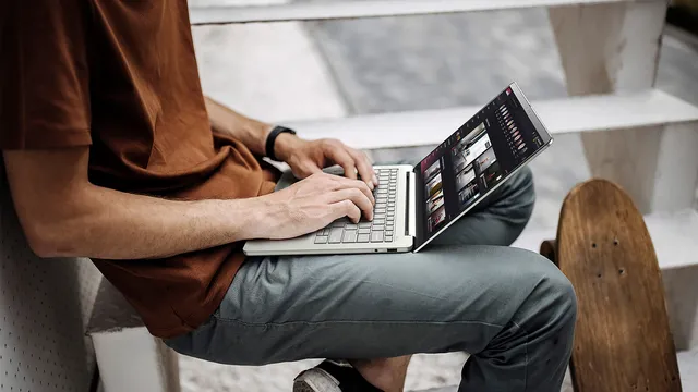 Homem sentado numa escada exterior a escrever num portátil Acer Swift Air 14 prateado pousado nas pernas, com um skate encostado ao lado