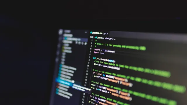 Ecrã de computador num ambiente escuro com linhas de código coloridas num editor, vistas em ângulo