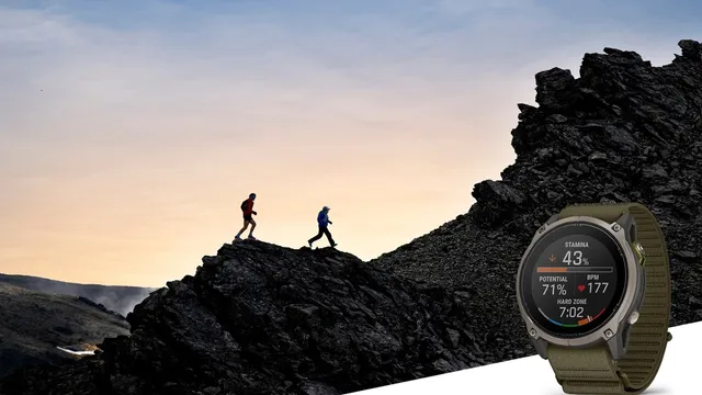 Duas pessoas a correr numa crista rochosa ao entardecer e, em primeiro plano, um relógio Garmin Enduro 4 com bracelete de tecido verde e o ecrã a mostrar a resistência e a frequência cardíaca