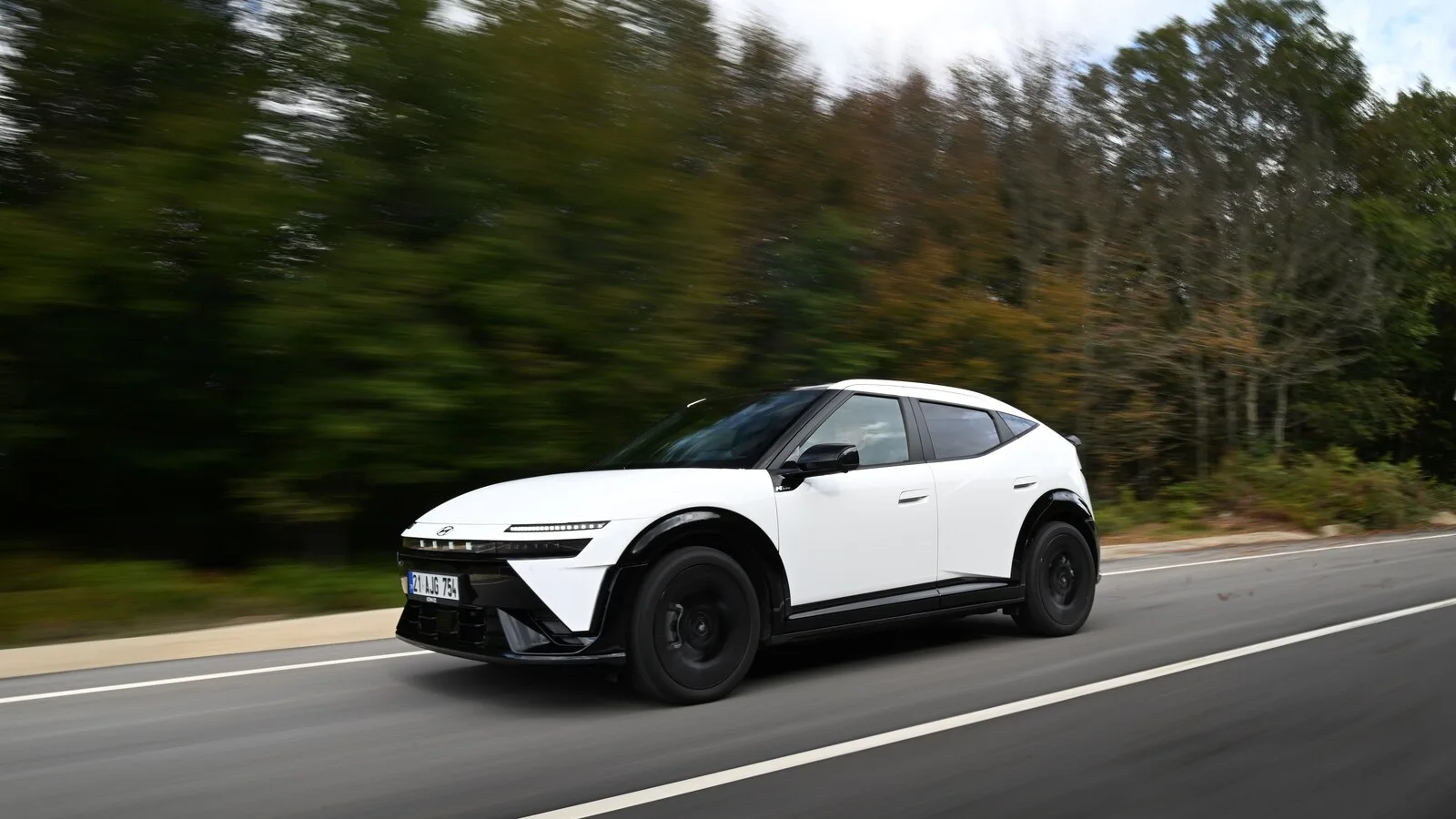 Hyundai Ioniq 3 branco com tejadilho preto a circular numa estrada ladeada de árvores, com o fundo desfocado pelo movimento