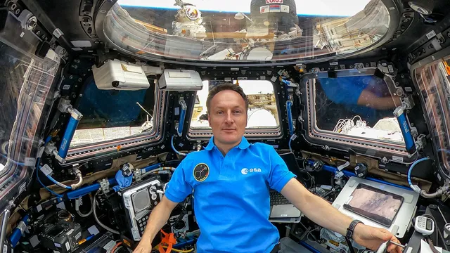 Matthias Maurer, de pólo azul da ESA, sentado na cúpula de sete janelas da Estação Espacial Internacional, rodeado de equipamento