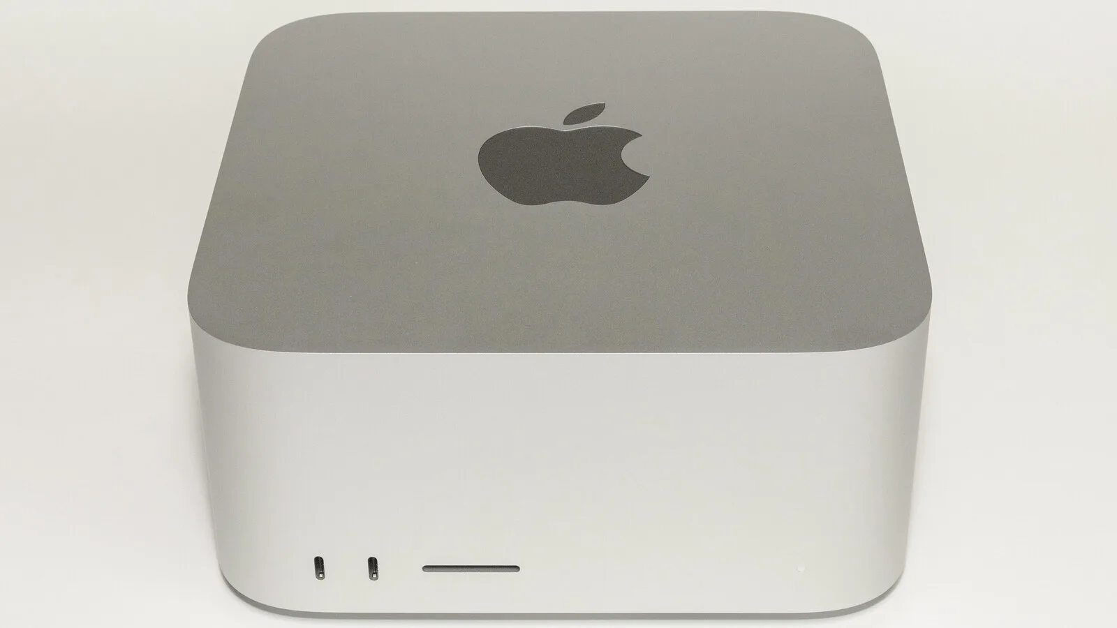 Computador Mac Studio prateado da Apple visto de frente, com o logótipo da maçã no topo e duas portas na parte da frente