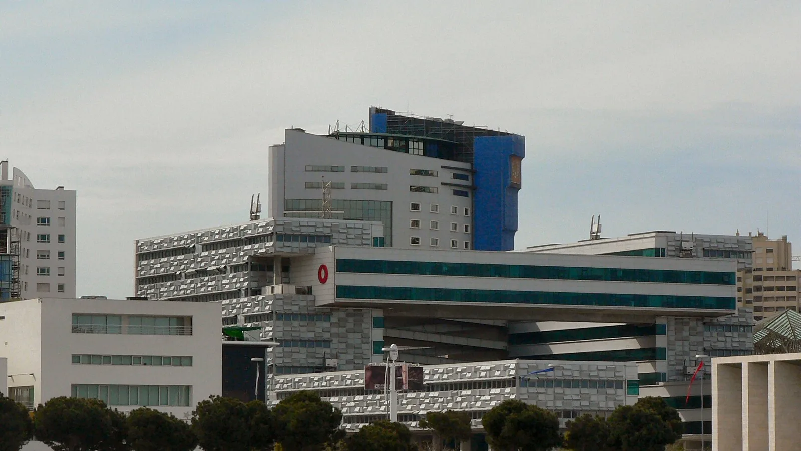 Edifício da Vodafone no Parque das Nações, em Lisboa, com fachada de faixas horizontais, rodeado por outros prédios e árvores