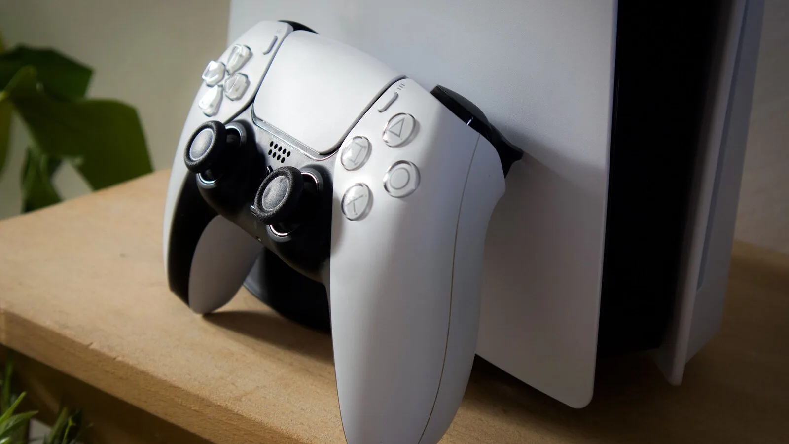 Comando DualSense branco encostado a uma consola PlayStation 5, numa prateleira de madeira