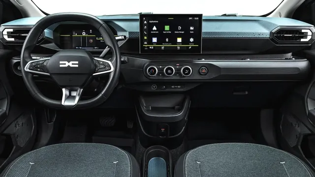 Tablier de um carro com volante de logótipo Dacia, painel de instrumentos digital, ecrã central com menu de aplicações e comandos da climatização