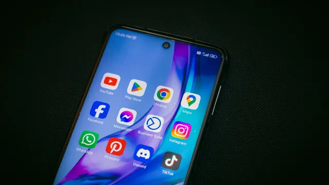Telemóvel Android pousado num fundo escuro, com o ecrã inicial cheio de ícones de aplicações como YouTube, Play Store, Chrome, Facebook, Instagram e TikTok