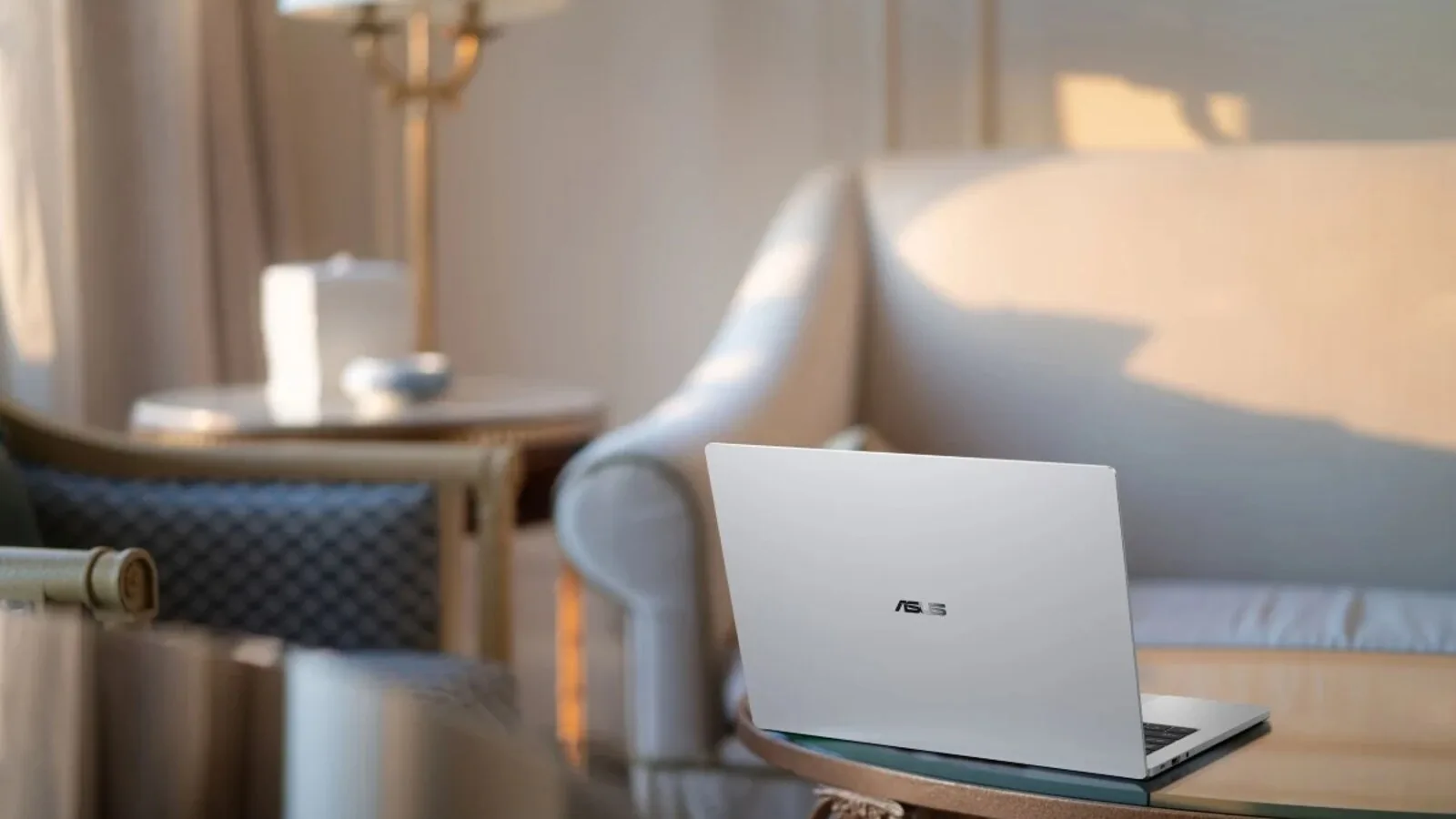 Portátil ASUS ExpertBook A7 prateado, aberto e visto de trás, pousado numa mesa redonda numa sala com sofá e candeeiro