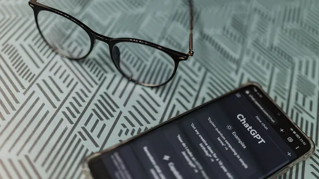 Telemóvel com a página do ChatGPT aberta no browser, pousado numa toalha às riscas ao lado de uns óculos