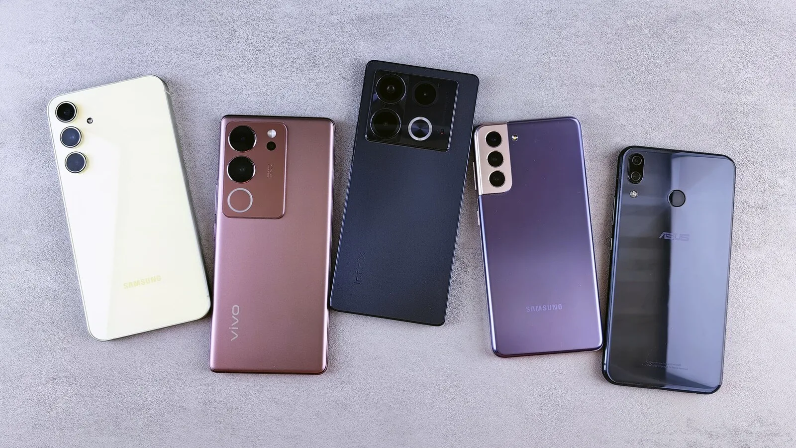 Cinco telemóveis de marcas diferentes, de costas e lado a lado sobre uma superfície cinzenta, com as câmaras traseiras à vista