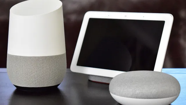 Coluna Google Home branca e cinzenta, ecrã Google Home Hub e coluna redonda Google Home Mini numa mesa escura