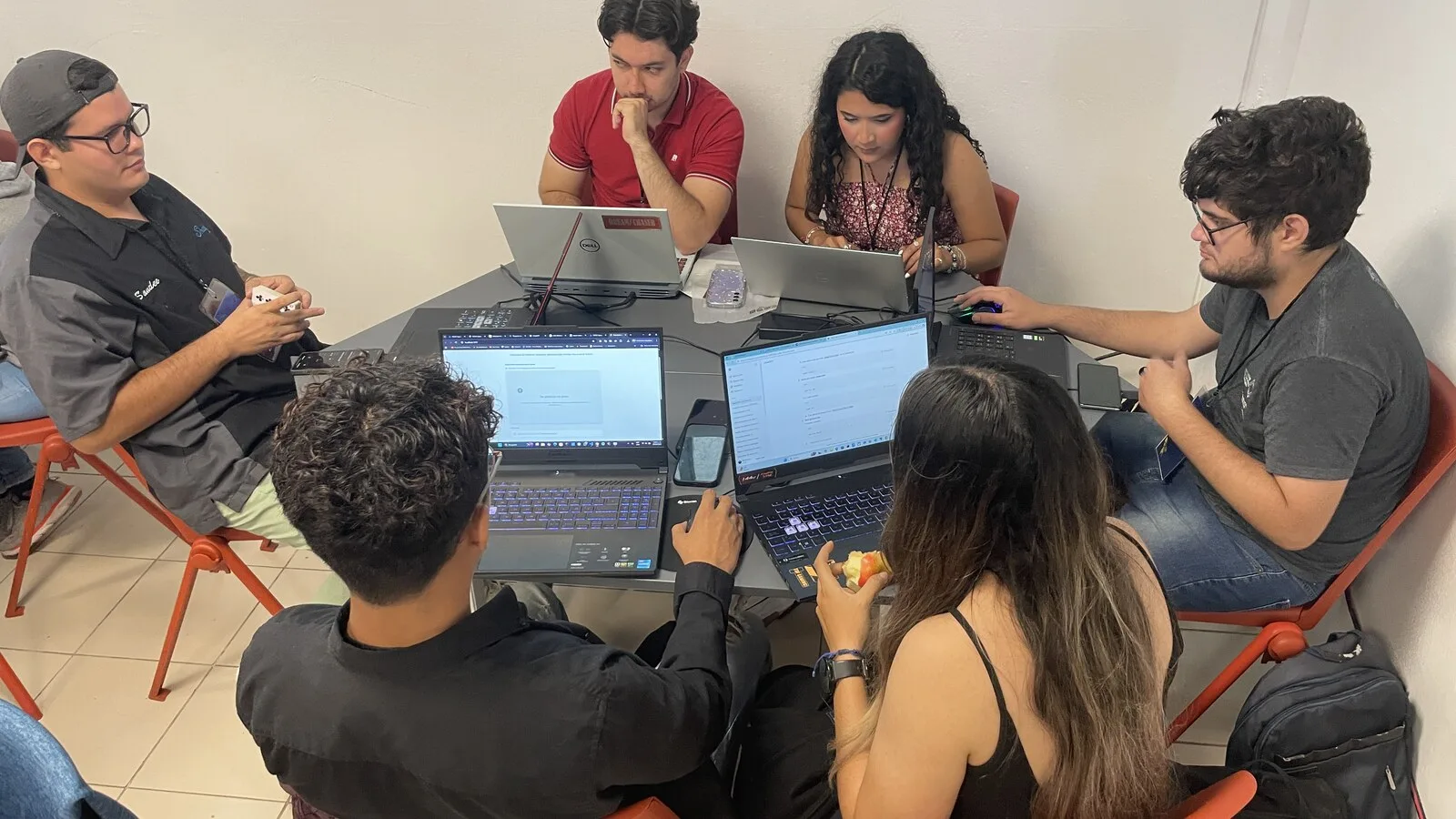 Seis jovens sentados à volta de uma mesa com vários portáteis abertos, durante uma maratona de programação