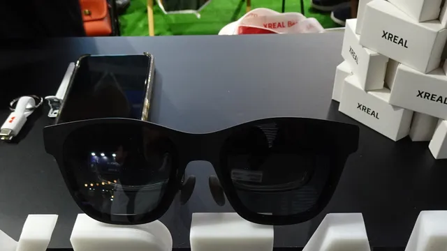 Óculos XREAL pretos numa banca de exposição, com um telemóvel e caixas da marca ao fundo