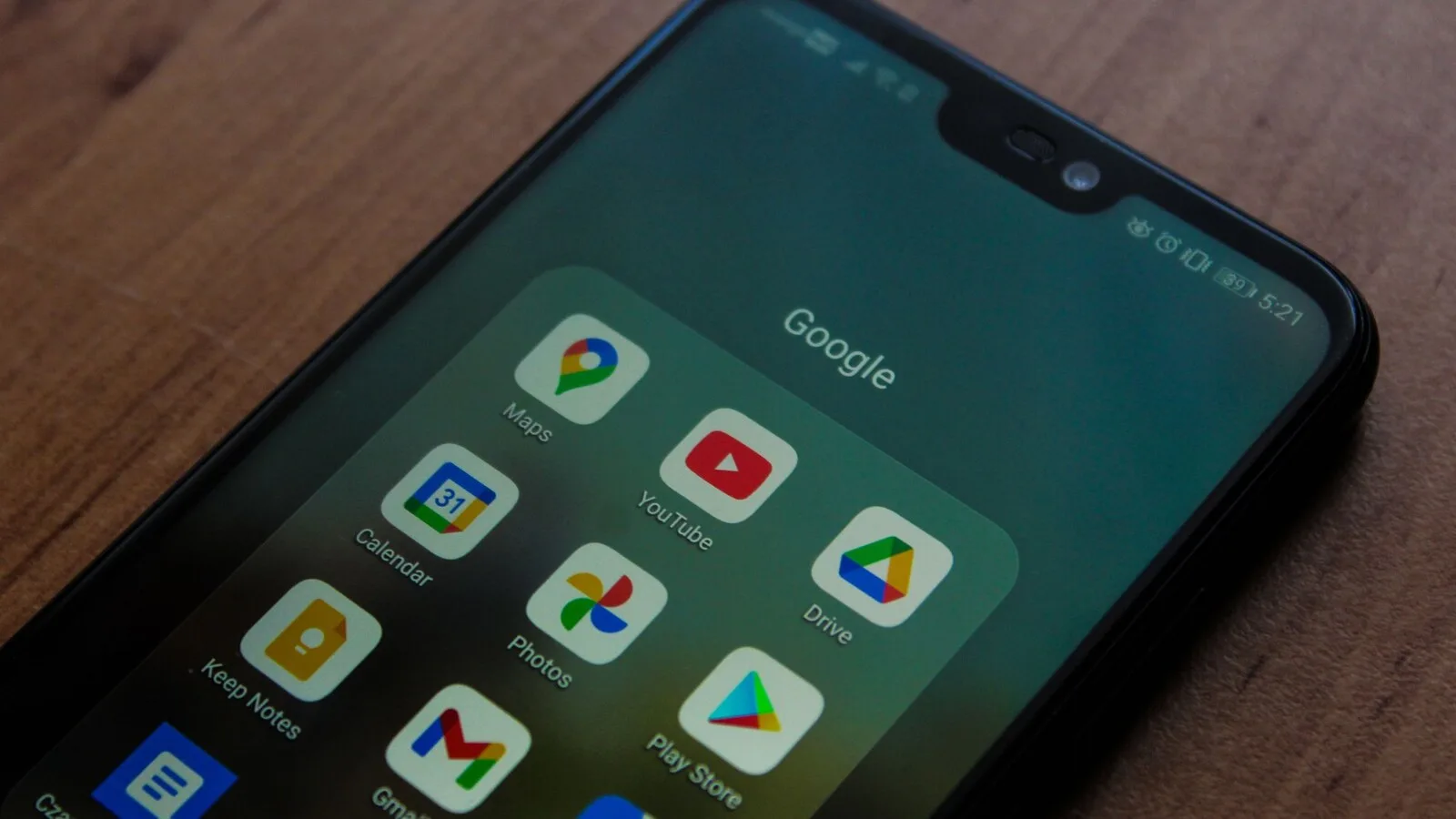 Telemóvel pousado numa mesa de madeira com uma pasta de aplicações da Google aberta no ecrã