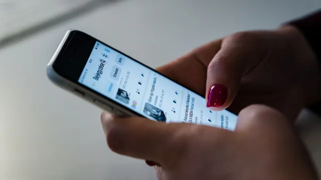 Mãos de uma mulher com unhas pintadas de vermelho a percorrer uma rede social num iPhone