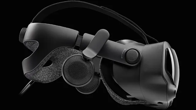 Óculo de realidade virtual Valve Index preto visto de lado sobre fundo escuro, com a fita de cabeça em tecido cinzento, os altifalantes afastados da cabeça e o cabo de ligação