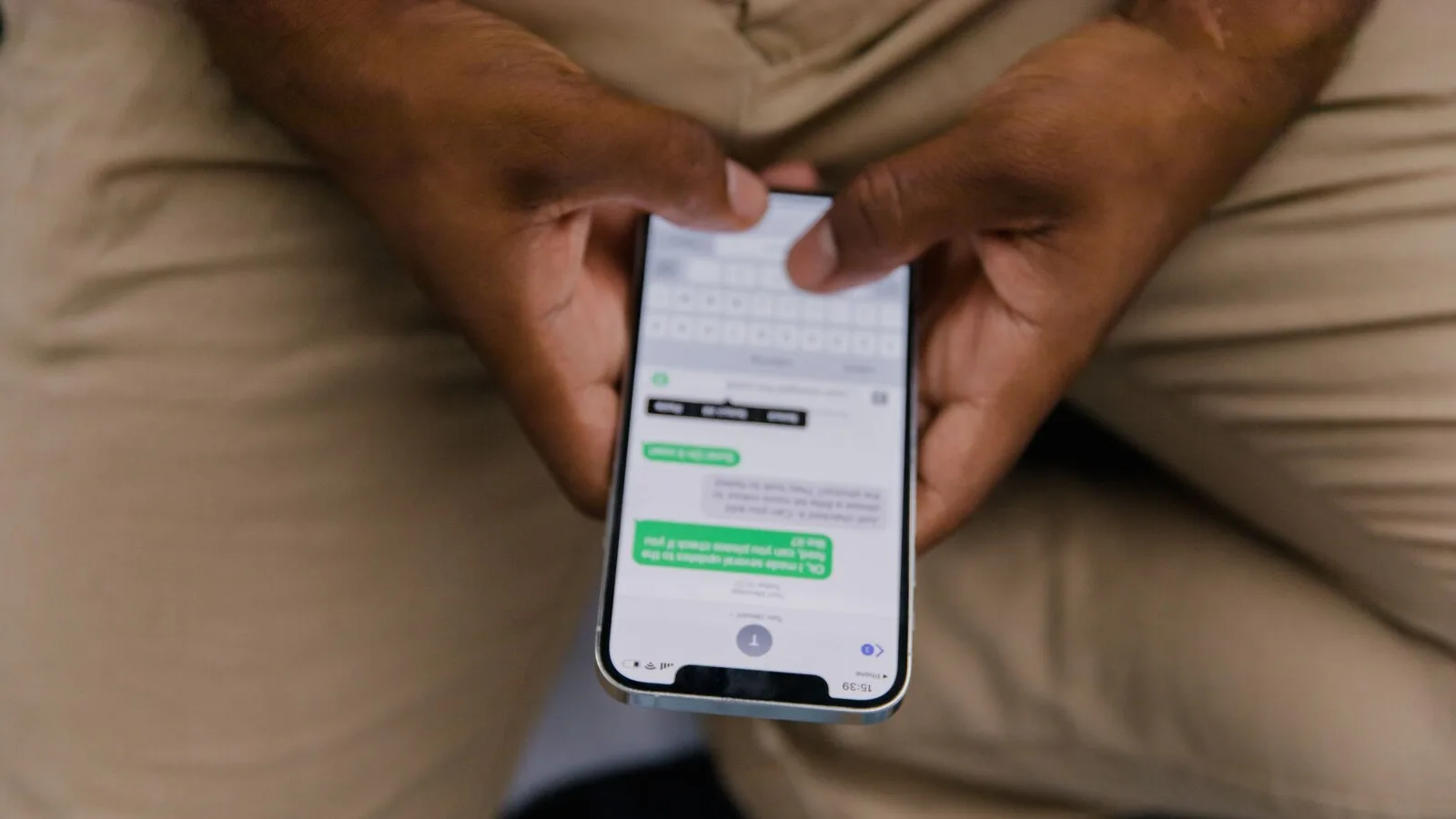 Mãos de um homem a segurar um iPhone com uma conversa de mensagens aberta no ecrã