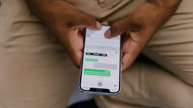Mãos de um homem a segurar um iPhone com uma conversa de mensagens aberta no ecrã