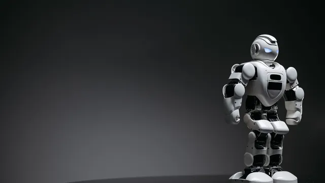 Pequeno robô de brinquedo branco e preto, de aspeto humanoide e olhos azuis acesos, sobre um fundo cinzento escuro
