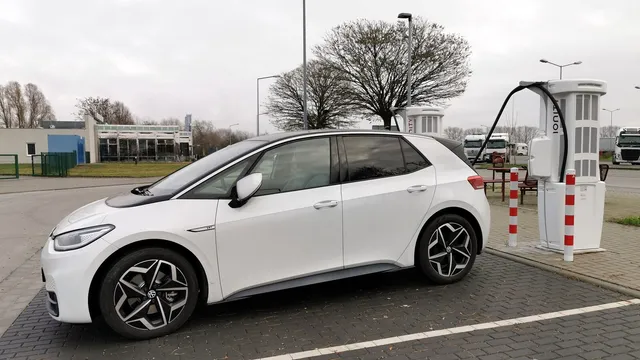 Volkswagen ID.3 branco estacionado junto a um posto de carregamento rápido, num parque de estacionamento com árvores sem folhas