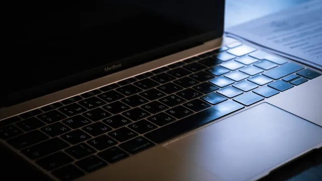 Grande plano do teclado de um MacBook numa secretária escura, iluminado de lado