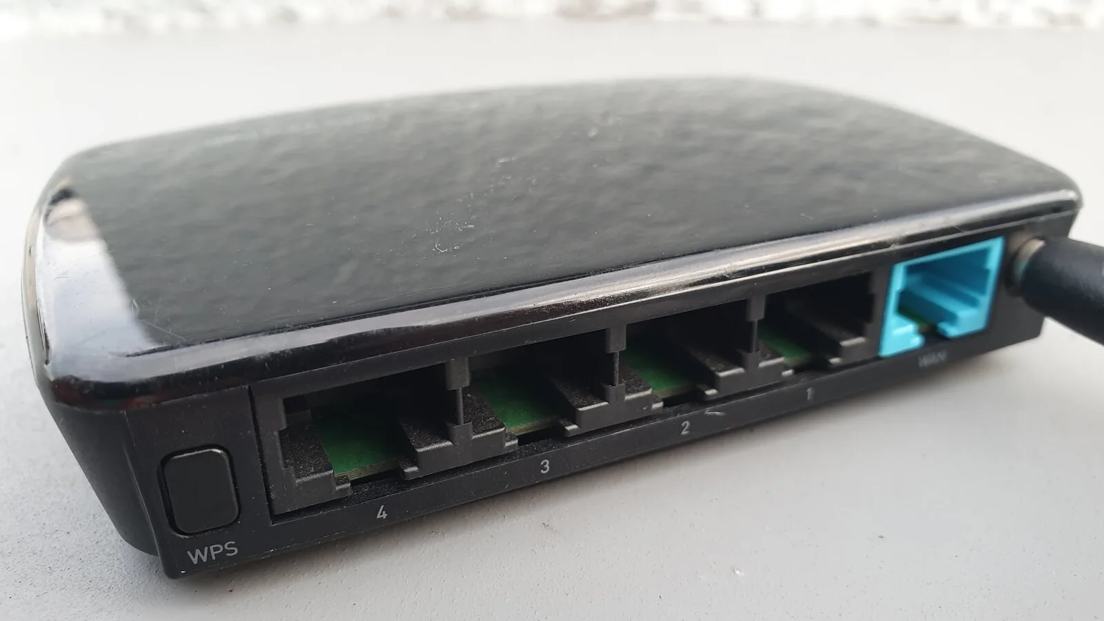 Traseira de um router preto com quatro portas de rede, uma porta WAN azul e um botão com a inscrição WPS