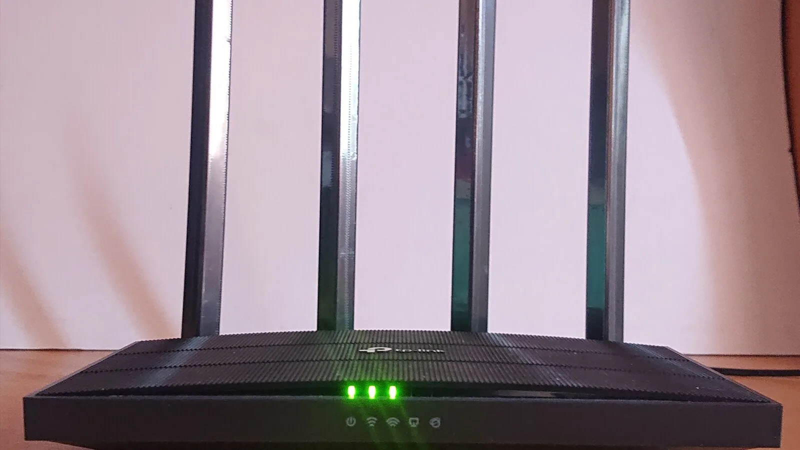 Router Wi-Fi preto com quatro antenas e luzes verdes acesas, pousado numa mesa de madeira